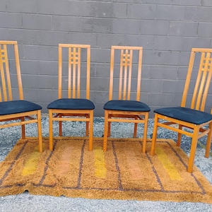 May include: A set of four wooden chairs with high backs featuring a grid pattern at the top and dark blue upholstered seats. The chairs have light brown wooden frames with straight legs and horizontal support bars between the legs for stability.