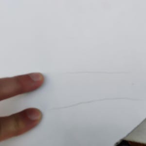 May include: A smooth white surface featuring two thin, parallel, light gray horizontal lines etched or drawn across the center. The surface appears flat and matte, with the lines providing a subtle, linear visual detail against the plain white background.