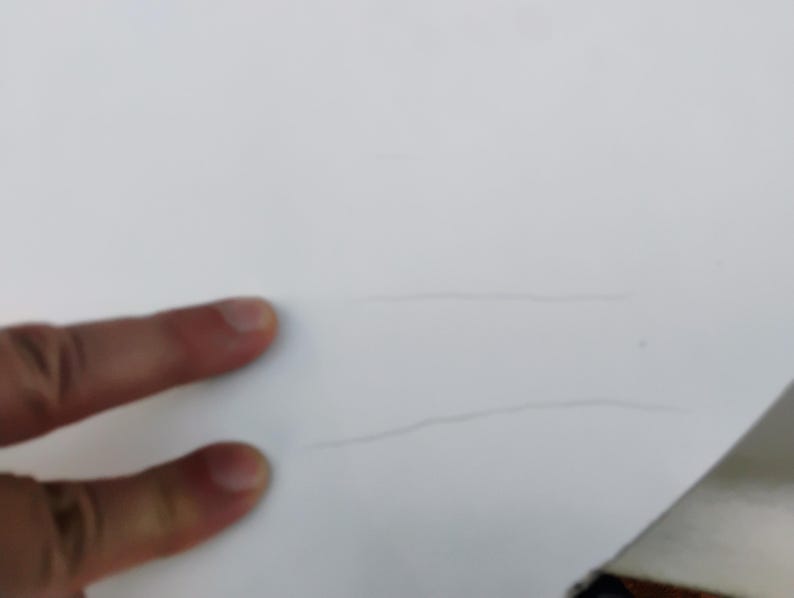 May include: A smooth white surface featuring two thin, parallel, light gray horizontal lines etched or drawn across the center. The surface appears flat and matte, with the lines providing a subtle, linear visual detail against the plain white background.