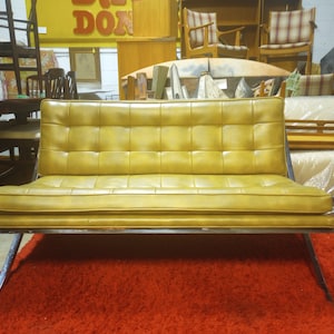 May include: A vintage yellow leather sofa with a tufted design and a metal frame. The sofa is sitting on a red rug.