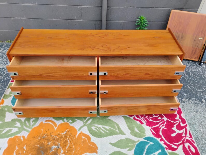 May include: A rectangular wooden dresser with a light brown finish featuring six open drawers arranged in two vertical columns. Each drawer is equipped with a rectangular silver metal pull handle on the left and right sides of the drawer front.