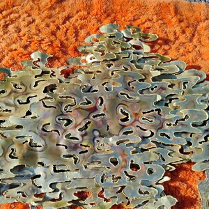 May include: A large, abstract wall sculpture made of layered, cut metal. The metal has a gold finish with iridescent hues and a textured, organic pattern.