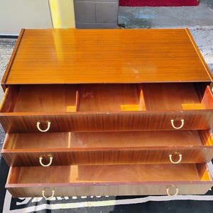 May include: A wooden dresser with three drawers and brass handles. The dresser is made of a light brown wood and has a smooth finish.