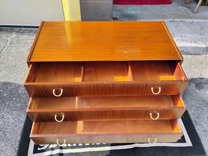 May include: A wooden dresser with three drawers and brass handles. The dresser is made of a light brown wood and has a smooth finish.