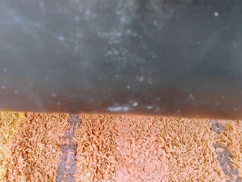 May include: A rectangular bath mat featuring a shaggy, textured pile in a striped pattern of muted orange, peach, and dark brown tones. The surface consists of dense, looped fibers that create a soft, uneven appearance across the entire mat.