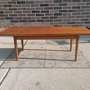 May include: A rectangular wooden coffee table with a warm brown finish, featuring a flat top surface with slightly raised edges and four tapered legs. The table is constructed from wood and displays a smooth, consistent grain pattern throughout.