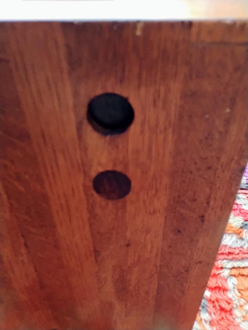 May include: Close-up of a wooden surface with two circular holes. The wood grain is visible, and the holes are dark, contrasting with the lighter wood. The image focuses on the texture and detail of the wood.