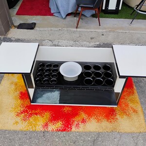 May include: A black and white bar cart with two fold-down serving trays and a built-in ice bucket. The cart has a black and white checkered pattern on the bottom.