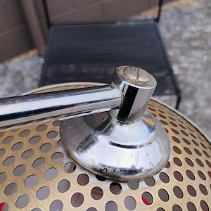 K&ouml;nnte beinhalten: Nahaufnahme einer Vintage-Lampe aus Chrom und Messing. Die Lampe hat einen perforierten Messingschirm mit einem Chromarm und -fu&szlig;. Die Lampe ist im Retro-Stil gestaltet.