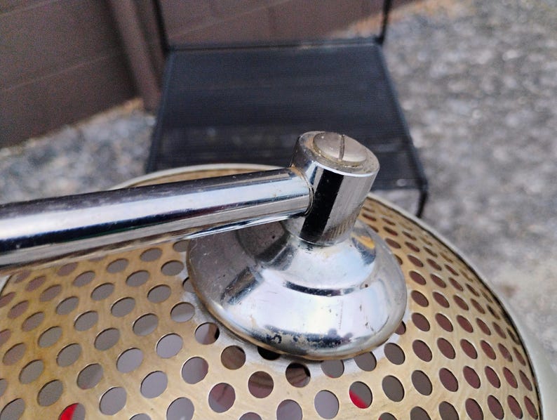 K&ouml;nnte beinhalten: Nahaufnahme einer Vintage-Lampe aus Chrom und Messing. Die Lampe hat einen perforierten Messingschirm mit einem Chromarm und -fu&szlig;. Die Lampe ist im Retro-Stil gestaltet.