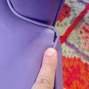 May include: Close-up of a purple leather chair with a tear in the seam. The chair is in front of a colorful rug.