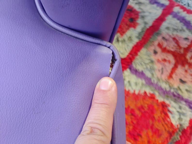 May include: Close-up of a purple leather chair with a tear in the seam. The chair is in front of a colorful rug.