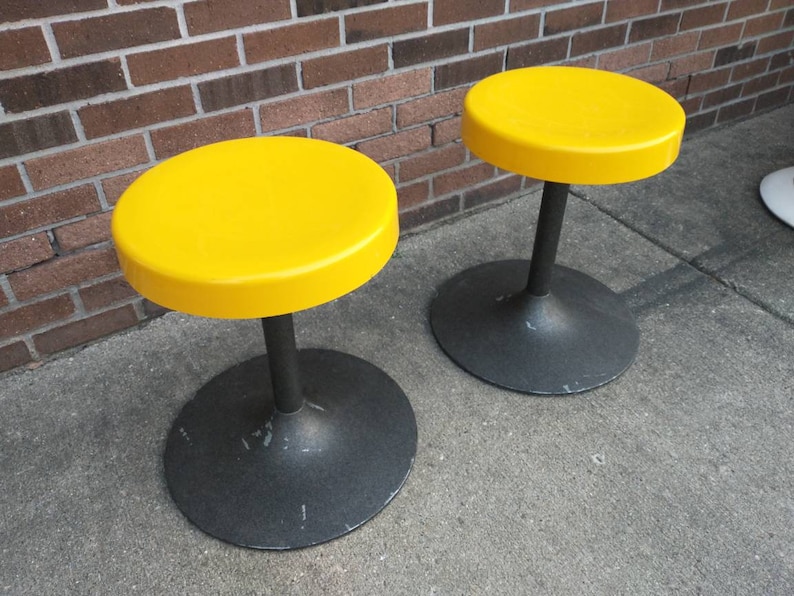 May include: Two yellow round stools with black bases. The stools are made of plastic and metal.