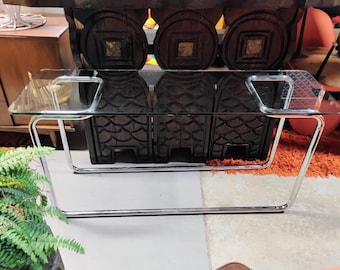 Könnte beinhalten: Ein Couchtisch aus klarem Glas mit rechteckiger Platte und verchromtem Metallrahmen. Der Tisch hat ein modernes Design und wird von gebogenen Beinen getragen. Der Tisch ist ca. 122 cm lang und 61 cm breit.