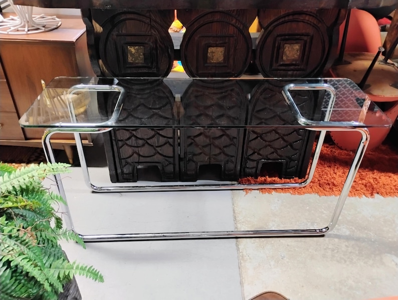 Peut inclure: Une table basse en verre transparent avec un plateau rectangulaire et un cadre en m&eacute;tal chrom&eacute;. La table a un design moderne et est soutenue par des pieds incurv&eacute;s. La table mesure environ 122 cm de long et 61 cm de large.