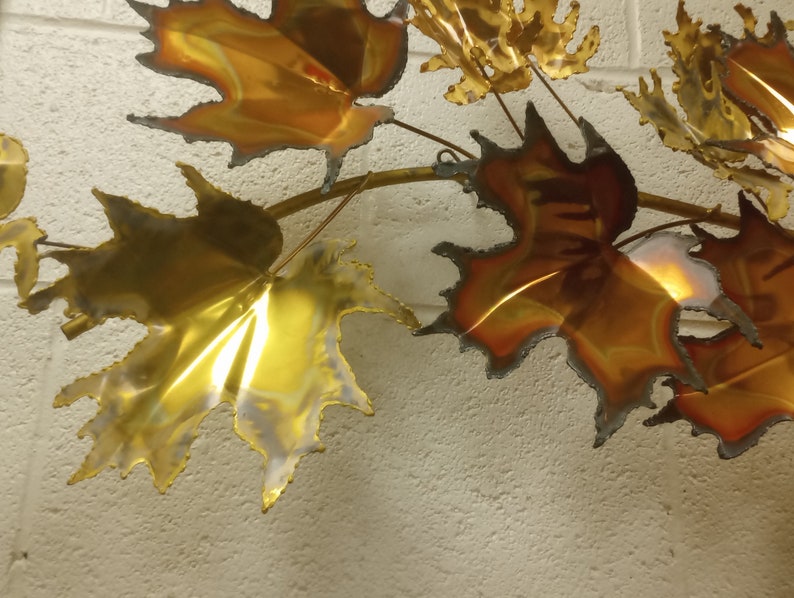 Puede incluir: Una escultura de pared hecha de hojas de metal en tonos dorados y cobrizos. Las hojas est&aacute;n dispuestas en cascada, creando una sensaci&oacute;n de movimiento y profundidad.