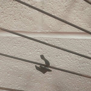 May include: A close-up of a metal sculpture featuring multiple thin rods radiating outwards from a central point. The rods are arranged in a radial pattern, giving the impression of movement and energy. The sculpture is crafted from a dark metal, potentially iron or steel, and has a rustic, industrial look.