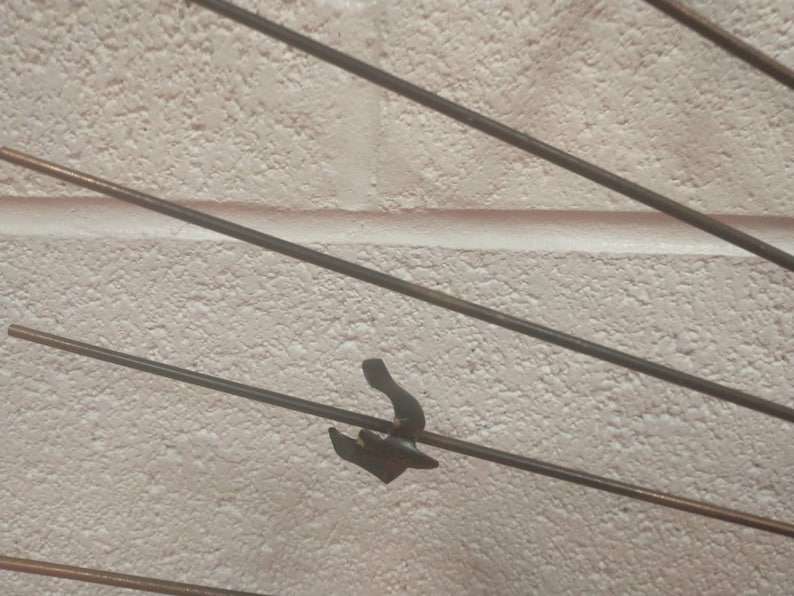 May include: A close-up of a metal sculpture featuring multiple thin rods radiating outwards from a central point. The rods are arranged in a radial pattern, giving the impression of movement and energy. The sculpture is crafted from a dark metal, potentially iron or steel, and has a rustic, industrial look.