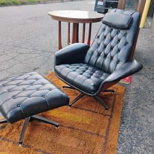May include: A black tufted lounge chair with a matching ottoman, both featuring button detailing and a headrest. The chair and ottoman are supported by silver-toned metal swivel bases with four legs, providing a stable foundation for the seating.