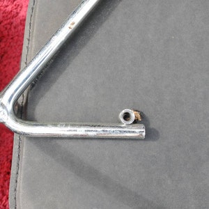 May include: A silver metal bike rack with a single arm extending out. The arm has a threaded end with a nut attached.