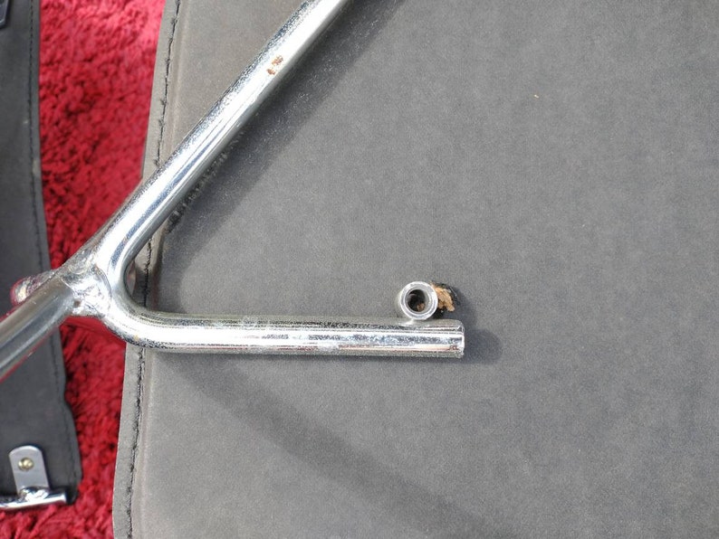 May include: A silver metal bike rack with a single arm extending out. The arm has a threaded end with a nut attached.