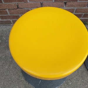 May include: A yellow round stool with a black base.