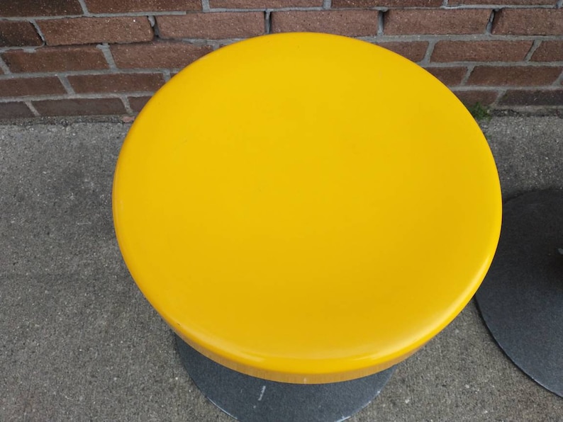 May include: A yellow round stool with a black base.