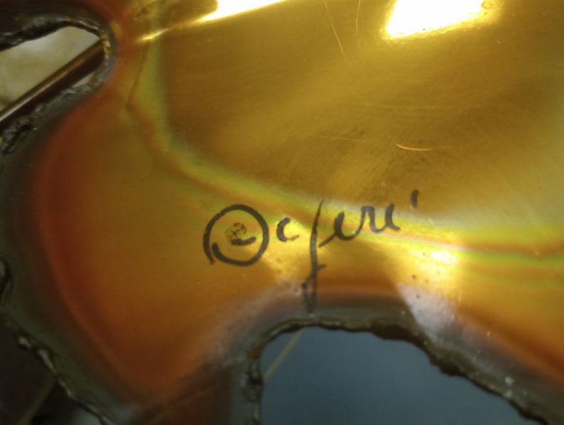 Puede incluir: Una escultura de metal de color dorado con una superficie rugosa y texturizada. La escultura est&aacute; firmada "Ocfuru" en tinta negra.
