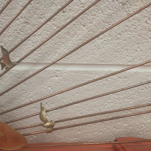May include: A wall sculpture made of metal with a sunburst design. The sculpture features multiple thin metal rods radiating outwards from a central point. There are three small bird-shaped metal accents attached to the rods.