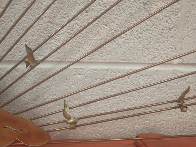 May include: A wall sculpture made of metal with a sunburst design. The sculpture features multiple thin metal rods radiating outwards from a central point. There are three small bird-shaped metal accents attached to the rods.