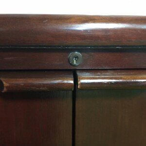 Pu&ograve; includere: Un armadio in legno scuro con due ante e un buco della serratura. L'armadio ha un design semplice con una finitura liscia.