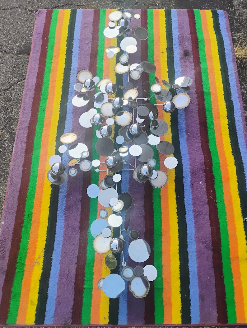 May include: A wall sculpture composed of numerous circular metal discs and spheres in polished chrome and silver finishes. The arrangement features varying sizes of reflective surfaces attached to a central metal frame, creating a cluster effect.