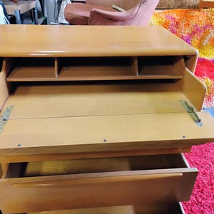 Op de afbeelding: Een licht houten bureau met een neerlaatbaar schrijfgedeelte en een lade. Het bureau heeft een aantal kleine planken boven het schrijfgedeelte.