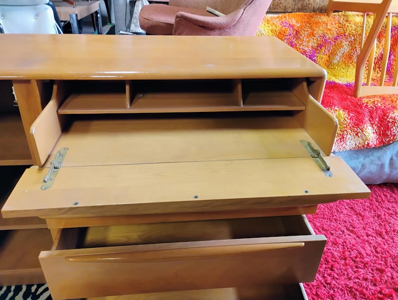 Op de afbeelding: Een licht houten bureau met een neerlaatbaar schrijfgedeelte en een lade. Het bureau heeft een aantal kleine planken boven het schrijfgedeelte.