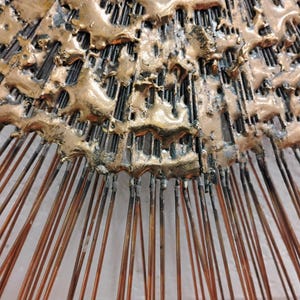 Puede incluir: Una escultura de pared de metal dorado con un dise&ntilde;o abstracto texturizado. La escultura tiene una forma circular con p&uacute;as radiantes.