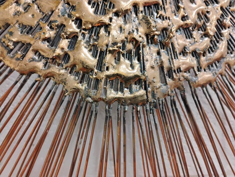 Puede incluir: Una escultura de pared de metal dorado con un dise&ntilde;o abstracto texturizado. La escultura tiene una forma circular con p&uacute;as radiantes.