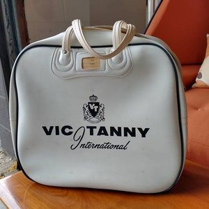 Pode incluir: Bolsa de viagem de couro branco com detalhes pretos e um logotipo preto que diz "VIC TANNY International".