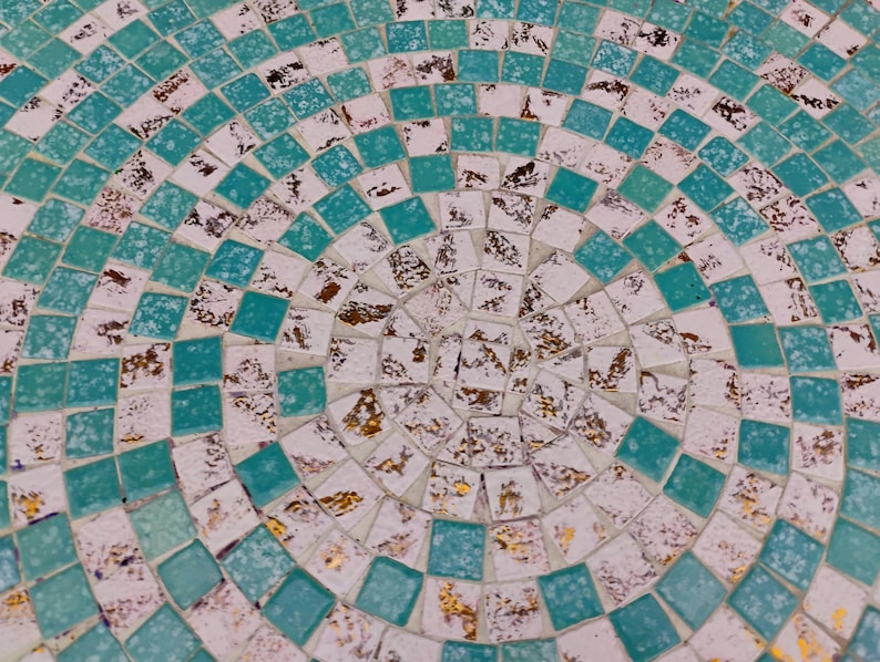 Op de afbeelding: Een cirkelvormig moza&iuml;ekpatroon met een witte achtergrond en turquoise blauwe tegels. Het midden van het patroon is een cirkel van gouden en witte tegels.