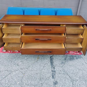 May include: A long wooden dresser with a smooth top surface, featuring three central drawers with horizontal handles and two side cabinets with three internal drawers each. The cabinet doors are open, revealing the interior storage compartments.