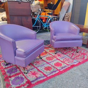 May include: Two purple chairs with a rounded back and a tufted seat. The chairs are on a red and purple rug.