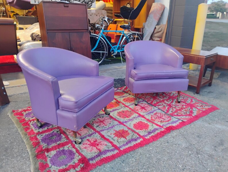 May include: Two purple chairs with a rounded back and a tufted seat. The chairs are on a red and purple rug.