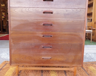 Könnte beinhalten: Eine Kommode im Stil der Mid-Century Modern mit sechs Schubladen und einer Holzoptik. Die Kommode hat ein schlichtes Design mit klaren Linien und dunkelbraunen Holzbeinen.