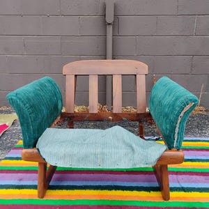 May include: A wooden chair frame featuring a curved backrest with three vertical slats, exposed metal coil springs, and two upholstered armrests in a textured teal fabric. A matching teal fabric seat cushion rests on the wooden base.