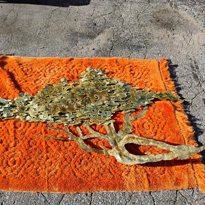 May include: A large gold metal wall sculpture in the shape of a tree with branches and leaves. The sculpture is on an orange rug.