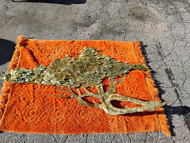 May include: A large gold metal wall sculpture in the shape of a tree with branches and leaves. The sculpture is on an orange rug.