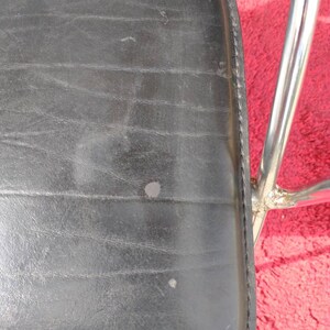 May include: Black leather chair seat with a chrome frame. The seat has a stitched edge and shows signs of wear.