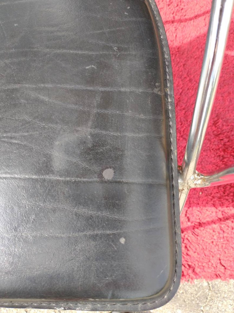 May include: Black leather chair seat with a chrome frame. The seat has a stitched edge and shows signs of wear.