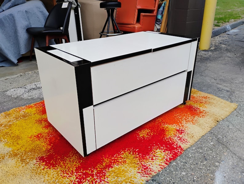 May include: White dresser with two drawers and black trim. The dresser is sitting on a colorful rug.