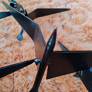 May include: Black metal decorative garden art featuring a stylized bird design. The artwork has a sleek, modern aesthetic with sharp angles and a matte finish. The bird's wings and tail are clearly defined, creating a dynamic visual effect. The piece is designed to be placed outdoors.