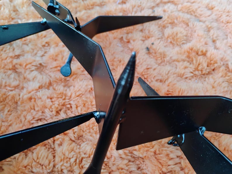 May include: Black metal decorative garden art featuring a stylized bird design. The artwork has a sleek, modern aesthetic with sharp angles and a matte finish. The bird's wings and tail are clearly defined, creating a dynamic visual effect. The piece is designed to be placed outdoors.